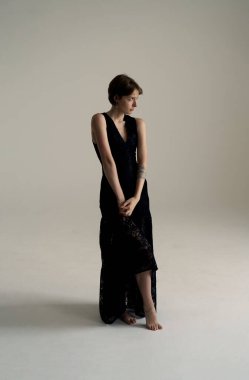 Resmi siyah cüppeli şık esmer manken dramatik ışıklandırmasıyla minimalist stüdyoda zarif bir şekilde duruyor.