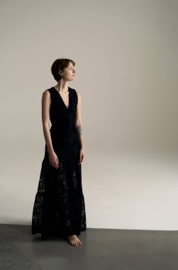 Kolsuz siyah elbiseler içinde şık bir model minimalist stüdyoda kendine güvenerek duruyor.