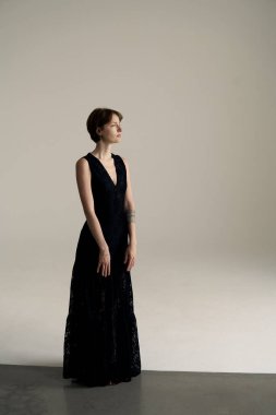 Dalgalı siyah elbiseli zarif kadın dramatik gölgelerle üç dörtlük stüdyo fotoğrafında yakalandı.