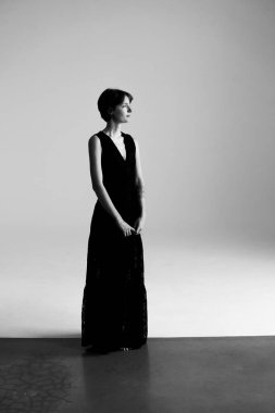 Sofistike siyah gece elbisesi içinde zarif bir esmer. Uzun stüdyo fotoğrafında yumuşak ışıklandırmayla çekilmiş.