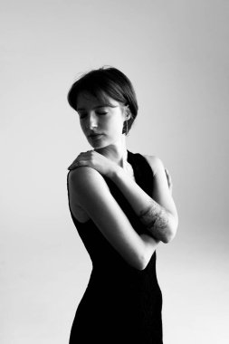 Zarif stüdyo ortamında çapraz kollu şık modelin profesyonel siyah beyaz portresi.