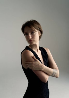 Minimalist stüdyoda siyah resmi giyinmiş, kollarını kavuşturarak poz veren sofistike esmer model.