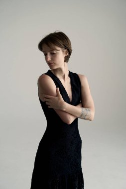 Kolsuz siyah elbiseli, minimalist stüdyoda kolları çapraz duran kendine güvenen bir manken.