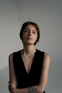 Hafif doğal ışıklandırma ve nötr arkaplan ile siyah kolsuz üst giyen düşünceli genç bir kadının portresi.