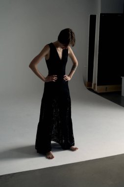 Zarif siyah gece elbisesi içindeki manken, geometrik gölgeli modern minimalist stüdyoda güvenle poz veriyor.