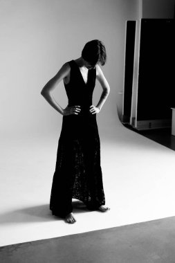 Akan siyah elbiseli zarif kadın dramatik ışıklandırmalı beyaz stüdyo duvarına karşı sanatsal bir siluet oluşturuyor.