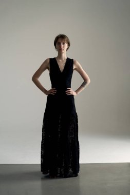 Siyah kolsuz elbise giyen profesyonel bir model. Parlak stüdyo ortamında elleri kalçalarında poz veriyor.