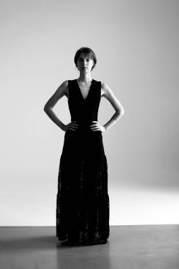 Klasik siyah elbiseli genç kadın profesyonel stüdyo ortamında kendine güvenen pozlar veriyor.