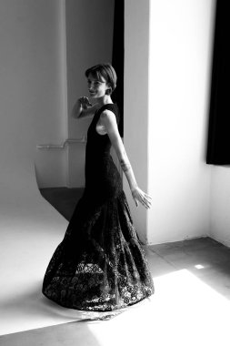 Siyah dantel elbiseli zarif kadın geometrik stüdyo arkaplanına karşı yumuşak ışıklandırmalı dramatik bir siluet oluşturuyor.