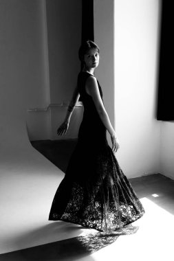 Uçan siyah cüppeli zarif kadın modern beyaz stüdyo duvarlarına karşı doğal pencere ışığı ile dinamik bir hareket yakalıyor.