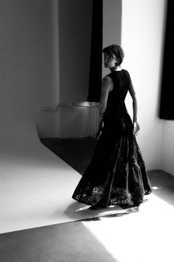 Moda modeli akıcı siyah elbise modern mimari stüdyosunda çarpıcı gölge oyunlarıyla dramatik siluet oluşturur.