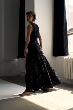 Zarif siyah gece elbisesi içindeki profesyonel model kıvrımlı mimari özellikleri olan parlak çağdaş stüdyoda zarifçe poz veriyor.