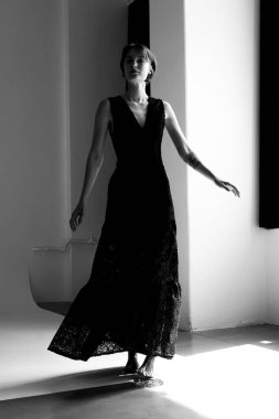 Sofistike siyah elbiseli zarif kadın geometrik ışık desenli çağdaş mimari stüdyoda zarif bir hareket yakalıyor.