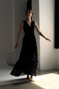 Siyah gece elbisesi içindeki manken dramatik doğal ışık ile modern stüdyo mimarisine karşı dinamik bir poz oluşturur.