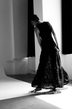 Dalgalı siyah gece elbisesi içindeki zarif kadın beton zemine karşı dinamik bir hareketi yakalıyor.