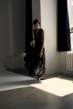 Siyah akşam giysisindeki sofistike model, geometrik ışık desenli çağdaş beton stüdyoda zarif bir poz verdi