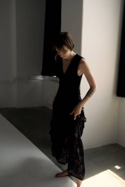 Zarif siyah gece elbisesi içindeki profesyonel model mimari özellikleri olan parlak çağdaş beton stüdyoda zarifçe poz veriyor.