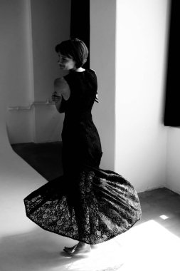 Süslü siyah dantelli elbisesiyle modern beyaz sanat alanında etkileyici bir hareket sergileyen zarif bir dansçı.