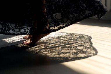 Süslü siyah dantelli kumaş ahşap zeminde doğal güneş ışığı bileşiminde dramatik gölgeler oluşturuyor.