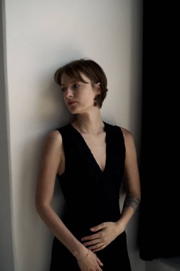 Gösterişli, siyah kolsuz bluzlu genç bir kadın minimalist beyaz duvar arkaplanına karşı güvenle poz veriyor.