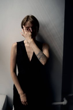 Çağdaş portre oturumunda siyah V yakalı şık bir kadın yüzüne dokunuyor.