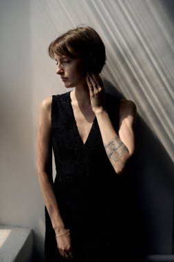 Çağdaş kadın portresi siyah kolsuz elbise içinde dramatik pencere ışığıyla sanatsal gölgeler yaratıyor.