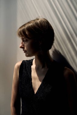 Siyah kolsuz kıyafetli zarif bir kadın sıcak altın saatli aydınlatmayla doğal pencere ışığında yakalandı.