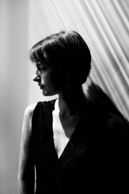 Gösterişli siyah giyimli, doğal ışıklandırma ve minimalist kompozisyonu olan zarif bir kadın portresi.