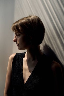 Dramatik yan profil portresi. Siyah kolsuz bluzlu, çarpıcı pencere gölgeleri olan kadın.