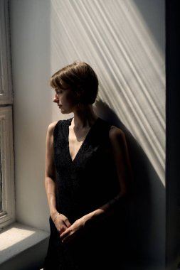 Çağdaş siyah kolsuz elbiseli kadın portresi dramatik pencere efektleriyle zarifçe oturuyor.