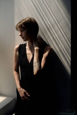 Siyah kolsuz bluzlu, dramatik yan ışıklandırmalı karamsar kadın portresi sanatsal gölge desenleri yaratıyor.