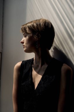 Siyah kolsuz elbise giymiş, altın saatinde ışıl ışıl ve zarif pozlu bir kadın portresi.