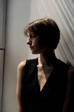 Siyah kolsuz bluzlu, yumuşak doğal ışıklandırması ve minimalist stüdyo arkaplanı olan bir kadının profesyonel vesikalığı.