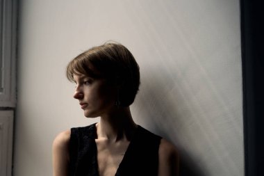 Siyah elbiseli genç bir kadının sanatsal portresi. Pencerenin kenarında doğal ışıklandırmayla oturuyor.