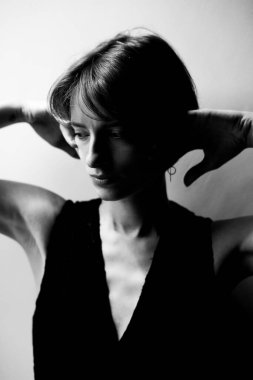 Siyah kolsuz bluzlu, ellerinin başının arkasında durduğu kadın portresi.