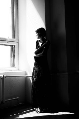 Siyah elbiseli bir kadının siluet portresi. Parlak pencere ışığıyla çerçevelenmiş.