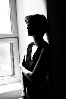 Siyah elbiseli kadının dramatik silüeti parlak pencere ışığına karşı