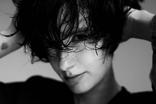 Черно-белый художественный портрет молодого человека с грязными волосами при мрачном освещении студии