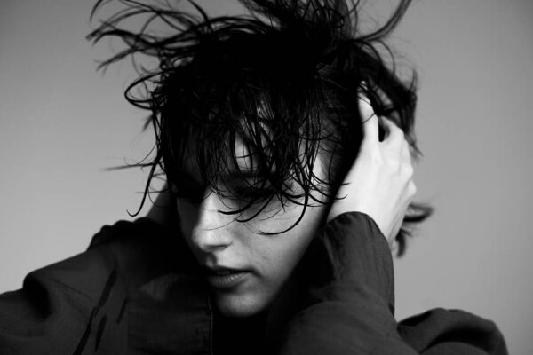 Черно-белый художественный портрет человека с грязными мокрыми волосами и выразительным жестом руки