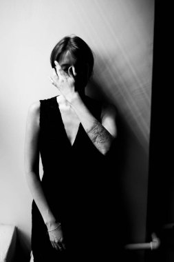 Tarafsız stüdyo arkaplanına karşı el hareketleriyle zarif siyah kıyafetli kendine güvenen bir kadının moda portresi.