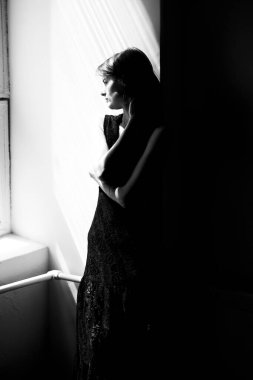 Siyah elbiseli, dramatik doğal ışıklandırmalı bir kadın silueti.