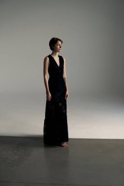 Uzun siyah elbiseli zarif model dramatik ışıklandırmalı geniş stüdyoda zarif duruyor.