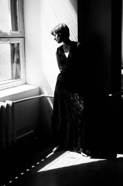 Dramatik pencere ışıklandırması ve mimari gölgeleri olan siyah elbiseli kadının sanatsal silueti.
