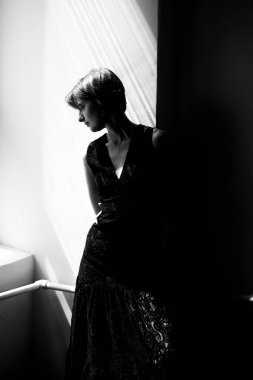 Pencere arkası aydınlatma ve minimalist kompozisyonu olan siyah elbiseli bir kadının silüet portresi