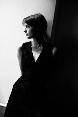 Siyah bluzlu, kısa saçlı, parlak pencere ışığında dramatik bir kadın silueti.