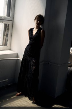 Parlak pencerenin önünde duran siyah elbiseli kadının uzun bir portresi.