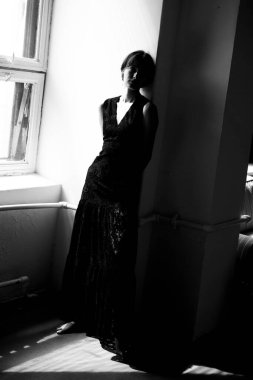 Siyah elbiseli zarif kadın pencereye karşı doğal ışıklandırmayla poz vermiş.