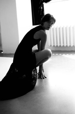 Siyah elbiseli sofistike bir kadın minimalist beyaz stüdyo zemininde zarif bir şekilde duruyor.