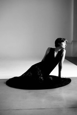 Siyah elbiseli kadının sanatsal portresi dramatik stüdyo ışıklarına karşı zarif bir şekilde yerleştirilmiş.