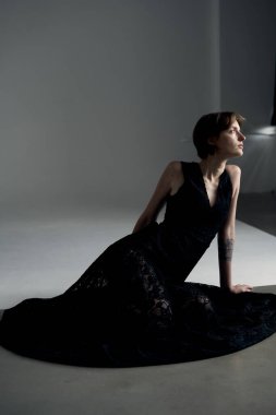 Siyah elbiseli çağdaş manken stüdyo ışıklarıyla dinamik poz veriyor.